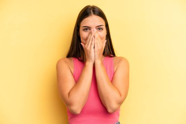 young adult pretty woman looking happy, cheerful, lucky and surprised covering mouth with both hands