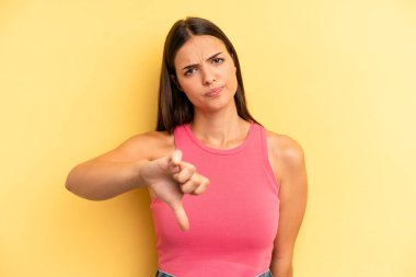 Genç ve güzel bir kadın sinirli, sinirli, hayal kırıklığına uğramış ya da hoşnutsuz, ciddi bir bakışla başparmağını kaldırıyor.