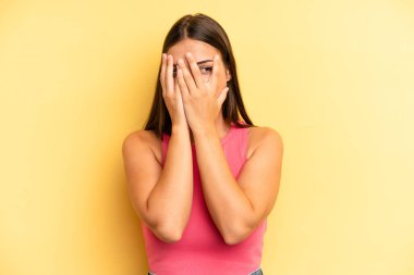 Genç ve güzel bir kadın elleriyle yüzünü kapatıyor, parmaklarının arasından şaşkın bir ifadeyle yan tarafa bakıyor.