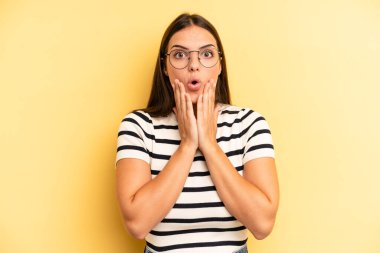 Genç ve güzel bir kadın şok olmuş ve korkmuş hissediyor, ağzı açık ve elleri yanaklarında korkmuş görünüyor.