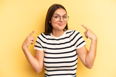 young adult pretty woman with a bad attitude looking proud and aggressive, pointing upwards or making fun sign with hands