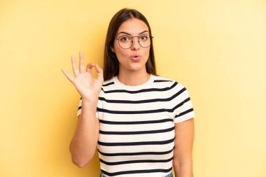 young adult pretty woman feeling successful and satisfied, smiling with mouth wide open, making okay sign with hand