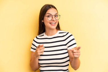 young adult pretty woman smiling with a positive, successful, happy attitude pointing to the camera, making gun sign with hands