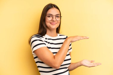 young adult pretty woman holding an object with both hands on side copy space, showing, offering or advertising an object