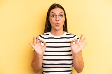 young adult pretty woman feeling shocked, amazed and surprised, showing approval making okay sign with both hands
