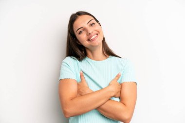 Genç ve güzel bir kadın kollarını kavuşturup mutlu bir şekilde gülüyor, rahat, pozitif ve tatmin edici bir pozla.
