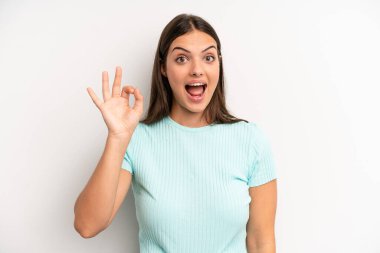 young adult pretty woman feeling successful and satisfied, smiling with mouth wide open, making okay sign with hand