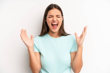 young adult pretty woman furiously screaming, feeling stressed and annoyed with hands up in the air saying why me