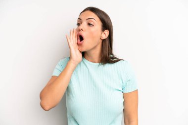 young adult pretty woman yelling loudly and angrily to copy space on the side, with hand next to mouth