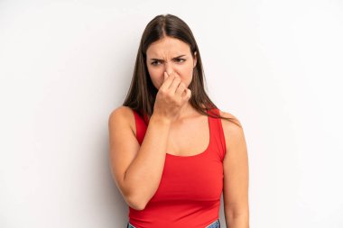 young adult pretty woman feeling disgusted, holding nose to avoid smelling a foul and unpleasant stench