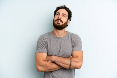 Genç sakallı adam mutlu, gururlu ve umutlu hissediyor, merak ediyor ya da düşünüyor, çapraz kollarla fotokopi çekmeyi bekliyor.