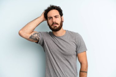 Genç, sakallı, kafası karışmış, başını kaşıyan ve yan tarafa bakan bir adam.