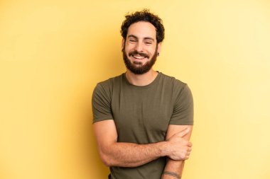 Genç, sakallı bir adam utangaç ve neşeli bir şekilde gülüyor, arkadaş canlısı, olumlu ama güvensiz bir tavırla.