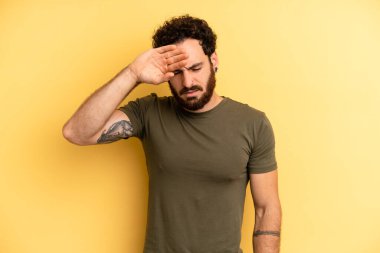 Genç, sakallı, stresli, yorgun ve hayal kırıklığına uğramış, alnından ter damlayan, umutsuz ve bitkin hisseden bir adam.