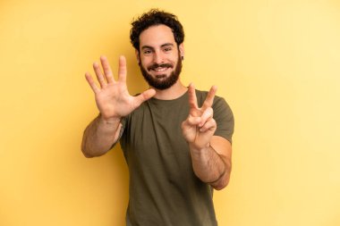 Genç, sakallı bir adam gülümsüyor ve dost canlısı görünüyor, 7 ya da 7 numarayı gösteriyor, eli önde, geriye doğru sayıyor.