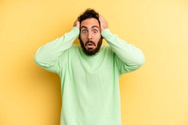 Genç, sakallı, heyecanlı ve şaşırmış görünen, ağzı açık, iki eli başında, kendini şanslı bir kazanan gibi hisseden bir adam.