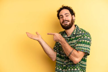 Genç, sakallı, neşeli bir şekilde gülümseyen ve yan taraftaki fotokopi alanını gösteren bir nesneyi gösteren ya da reklamını yapan bir adam.