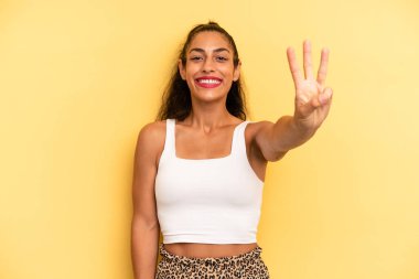 İspanyol güzel kadın gülümsüyor ve arkadaş canlısı görünüyor. Üç ya da üç numarayı gösteriyor. Elleri önde, geriye doğru sayıyor.