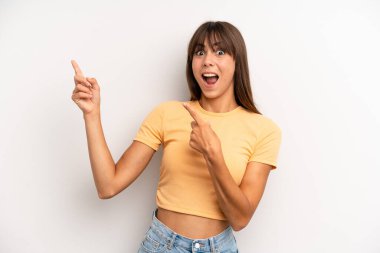 Hispanik güzel kadın neşeli ve şaşırmış hissediyor, şok olmuş bir ifadeyle gülümsüyor ve bir tarafı işaret ediyor.