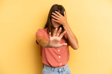 İspanyol asıllı güzel bir kadın elleriyle yüzünü örtüyor ve diğer elini kamerayı durdurmak için öne koyuyor, fotoğraf ya da resimleri reddediyor.