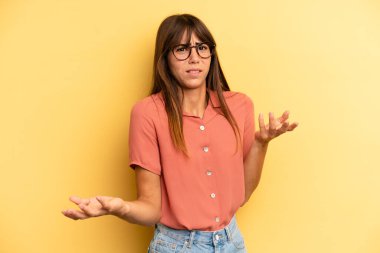 hispanic pretty woman shrugging with a dumb, crazy, confused, puzzled expression, feeling annoyed and clueless