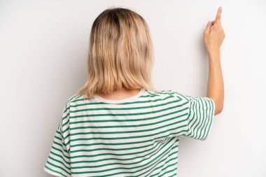young adult blonde woman standing and pointing to object on copy space, rear view