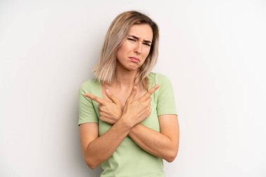 young adult blonde woman looking puzzled and confused, insecure and pointing in opposite directions with doubts
