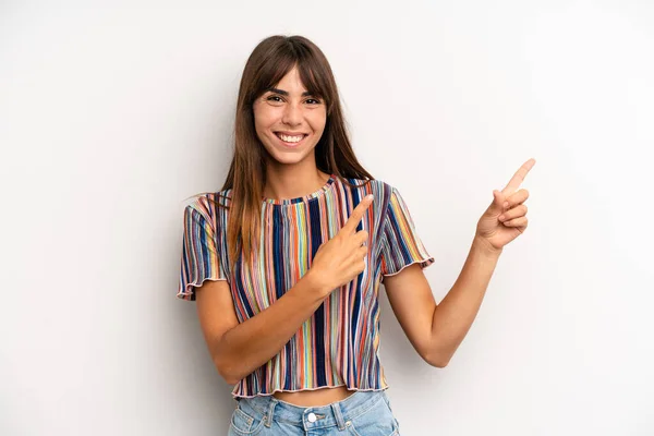 hispanic pretty woman smiling happily and pointing to side and upwards with both hands showing object in copy space