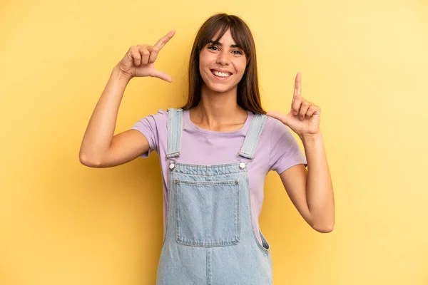 hispanic pretty woman framing or outlining own smile with both hands, looking positive and happy, wellness concept