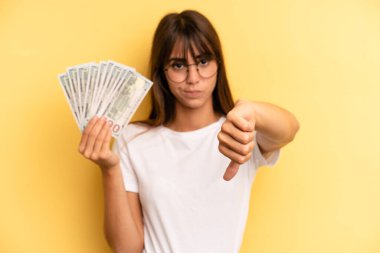 hispanic woman smiling and looking happy, gesturing victory or peace. dollar banknotes concept