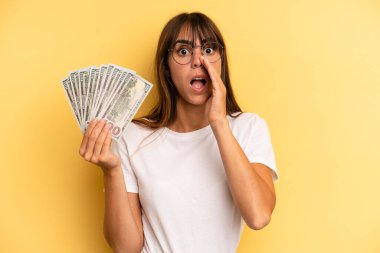 hispanic woman feeling happy,giving a big shout out with hands next to mouth. dollar banknotes concept