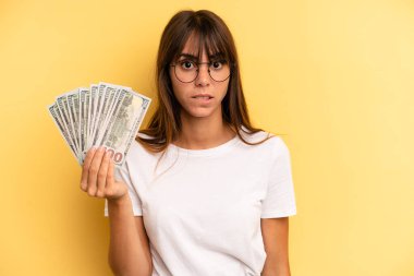 hispanic woman looking puzzled and confused. dollar banknotes concept