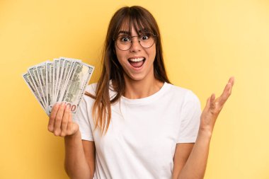 hispanic woman feeling extremely shocked and surprised. dollar banknotes concept