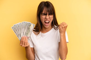 hispanic woman shouting aggressively with an angry expression. dollar banknotes concept