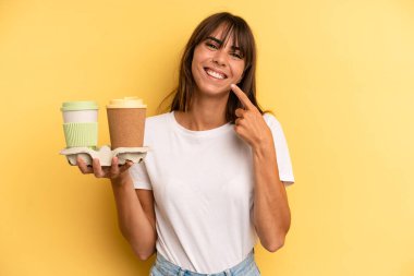 smiling confidently pointing to own broad smile. take away coffees