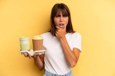 with mouth and eyes wide open and hand on chin. take away coffees