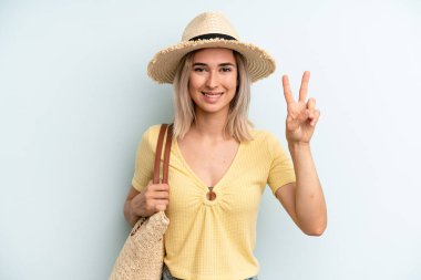 blonde woman smiling and looking happy, gesturing victory or peace. summer concept