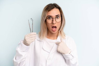 Şok olmuş ve ağzı açık, kendini gösteren sarışın bir kadın. dişçi kavramı