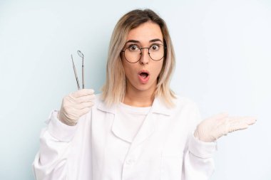 Sarışın kadın şaşırmış ve şok olmuş görünüyor. Çenesi düşmüş ve elinde bir nesne var. dişçi kavramı