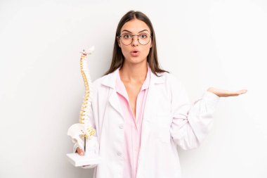 Güzel kadın şaşırmış ve şok olmuş görünüyor. Çenesi düşmüş ve elinde bir nesne tutuyor. Omurga uzmanı konsepti