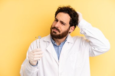 Genç adam şaşkın ve kafası karışmış hissediyor, başını kaşıyor. dişçi kavramı