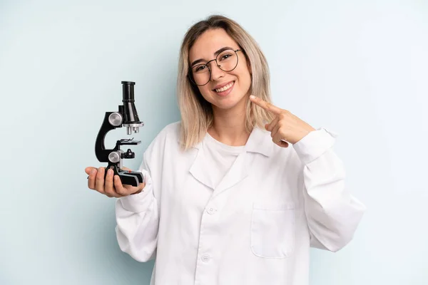 blonde woman smiling confidently pointing to own broad smile. scientist student concept