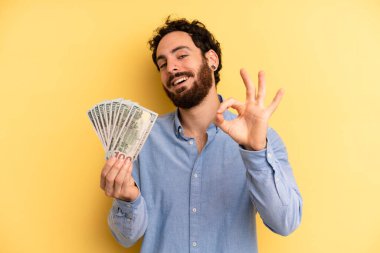 Genç adam kendini mutlu hissediyor, iyi bir jestle onaylıyor. Dolar banknotları konsepti
