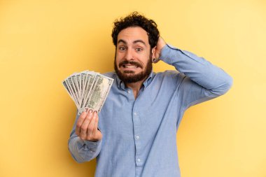 Genç adam stresli, endişeli ya da korkmuş hissediyor. Elleri başının üstünde. Dolar banknotları konsepti