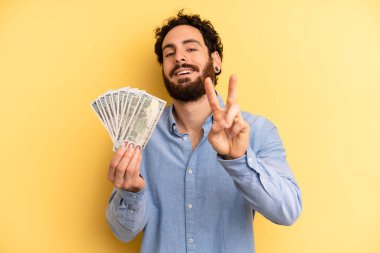 Genç adam gülümsüyor ve iki numarayı gösteriyor. Dolar banknotları konsepti
