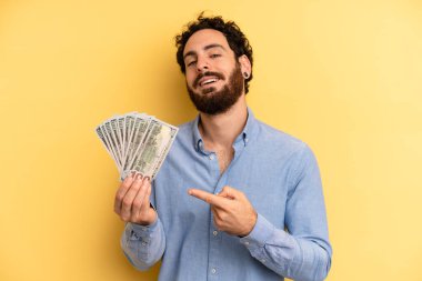 Genç adam neşeyle gülümsüyor, mutlu hissediyor ve bir tarafı işaret ediyor. Dolar banknotları konsepti