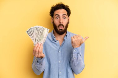 Genç adam inançsızlıktan şaşkın şaşkın bakıyor. Dolar banknotları konsepti