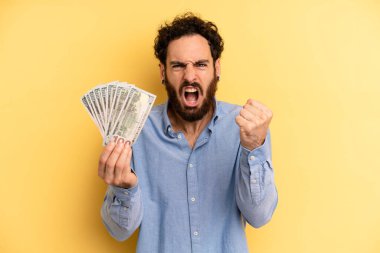 Genç adam öfkeli bir ifadeyle agresif bir şekilde bağırıyor. Dolar banknotları konsepti