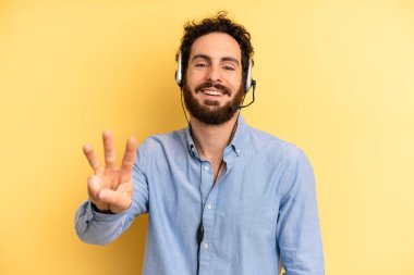 Genç adam gülümsüyor ve arkadaş canlısı görünüyor, üç numarayı gösteriyor. tele pazarlamacı kavramı