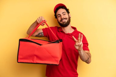 Genç adam gülümsüyor ve arkadaş canlısı görünüyor, üç numarayı gösteriyor. Pizza teslimatı kavramı